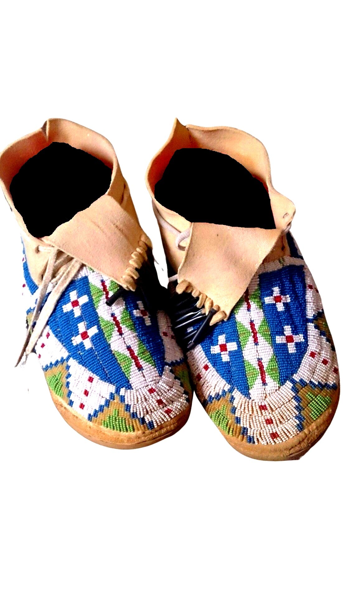 A pair of handmade beaded moccasins with a colorful geometric pattern, featuring a mix of blue, green, and yellow beads, and with the sole of the foot facing upwards.